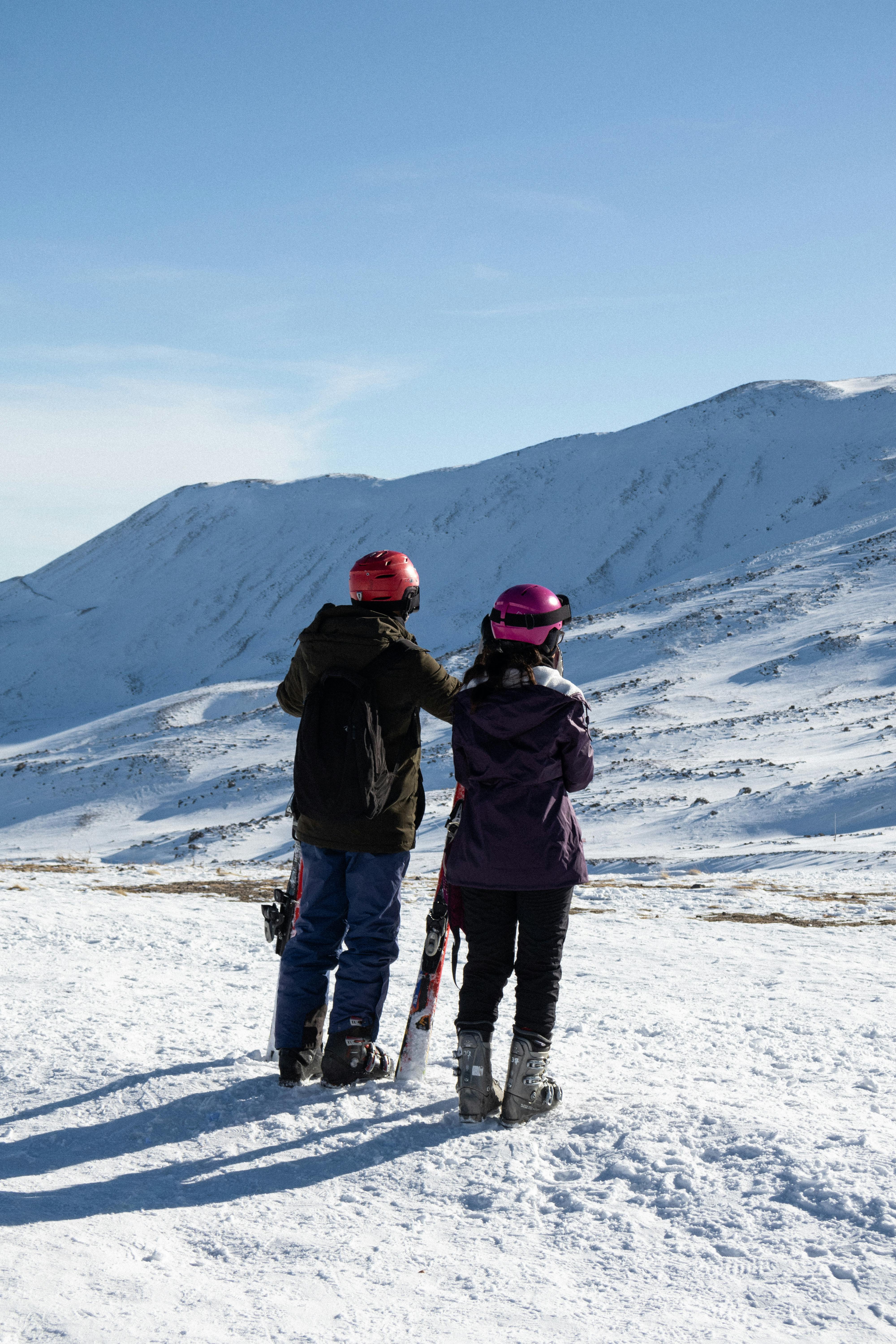 Two skiers in winter gear enjoy a snowy mountainous landscape with clear blue sky.