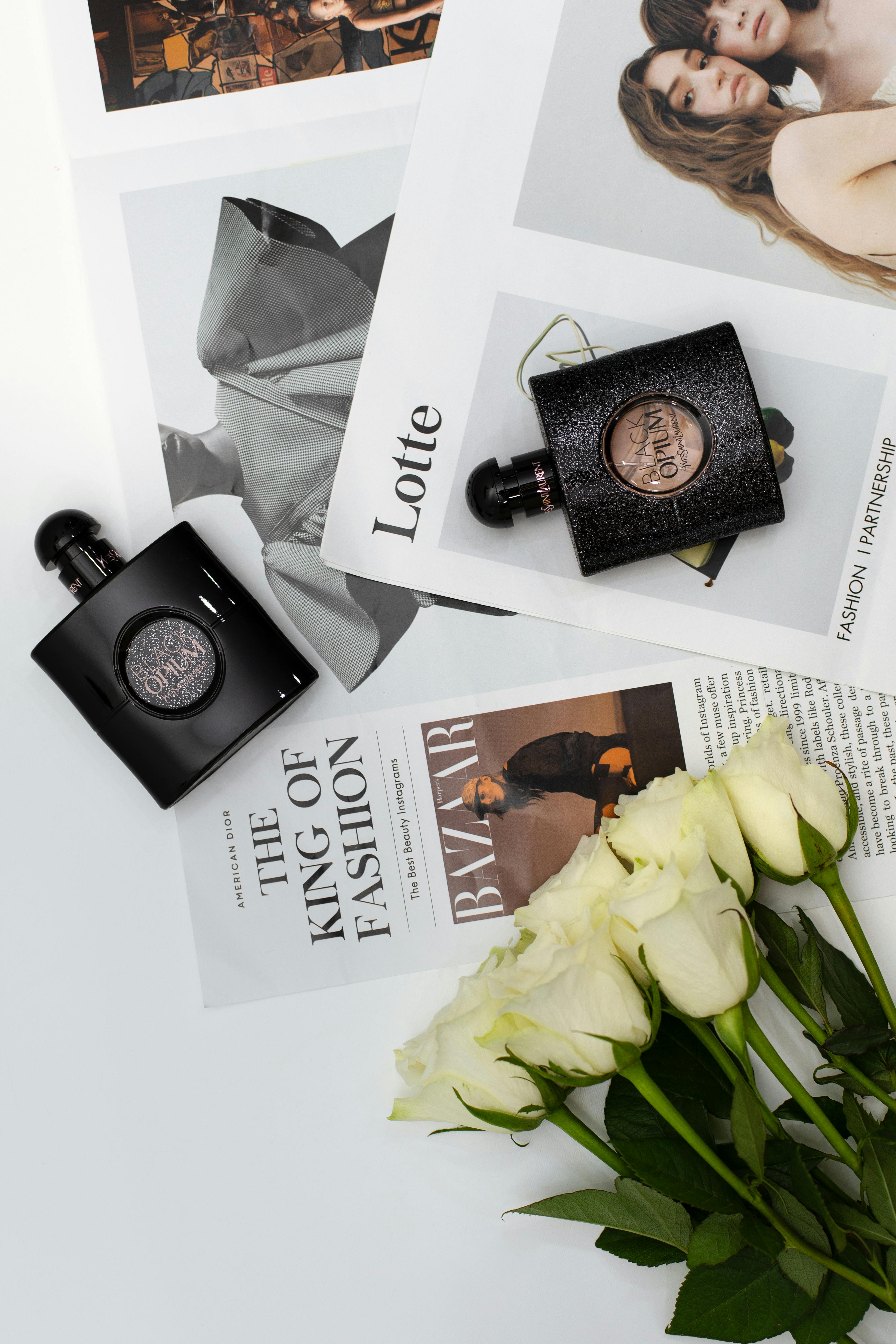 Perfume bottles displayed on fashion magazines with white roses, perfect for a chic lifestyle theme.
