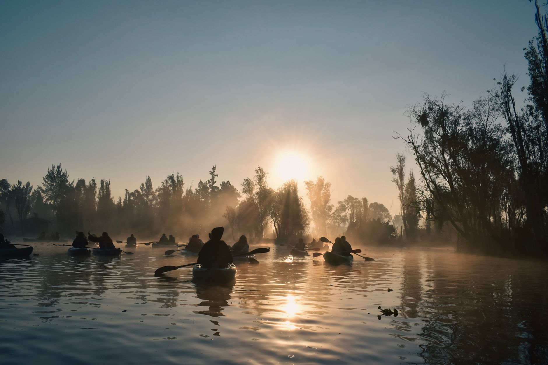 Silhouettes of kayakers paddling through Xochimilco canals at sunrise in Mexico City.