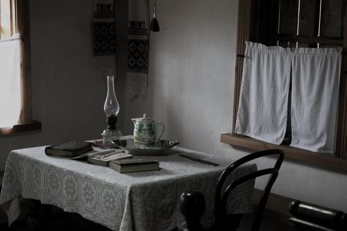 Free Cozy vintage dining room with books, oil lamp, and lace tablecloth. Stock Photo