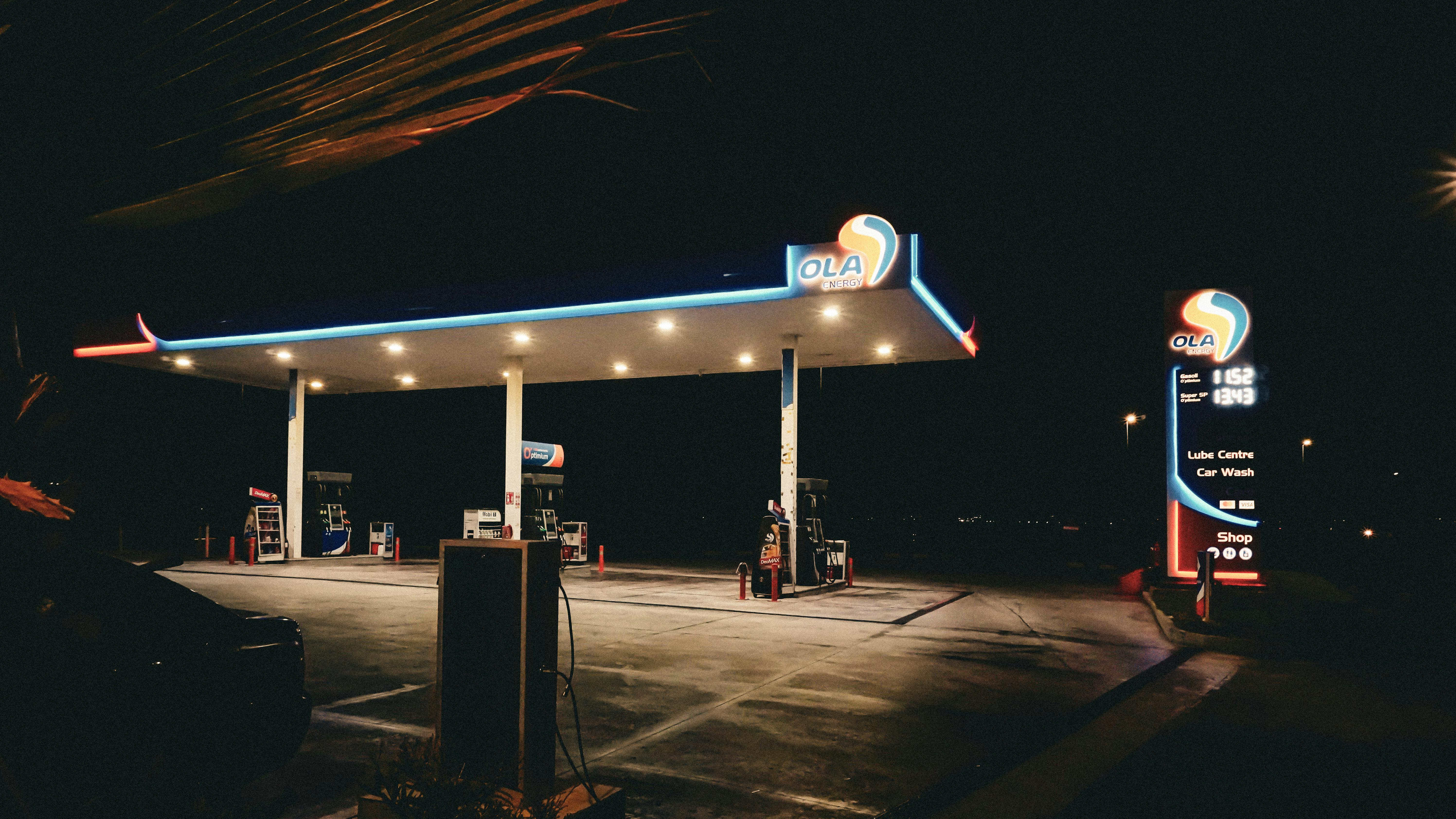 Night view of a lit-up gas station with glowing signage and empty pumps.