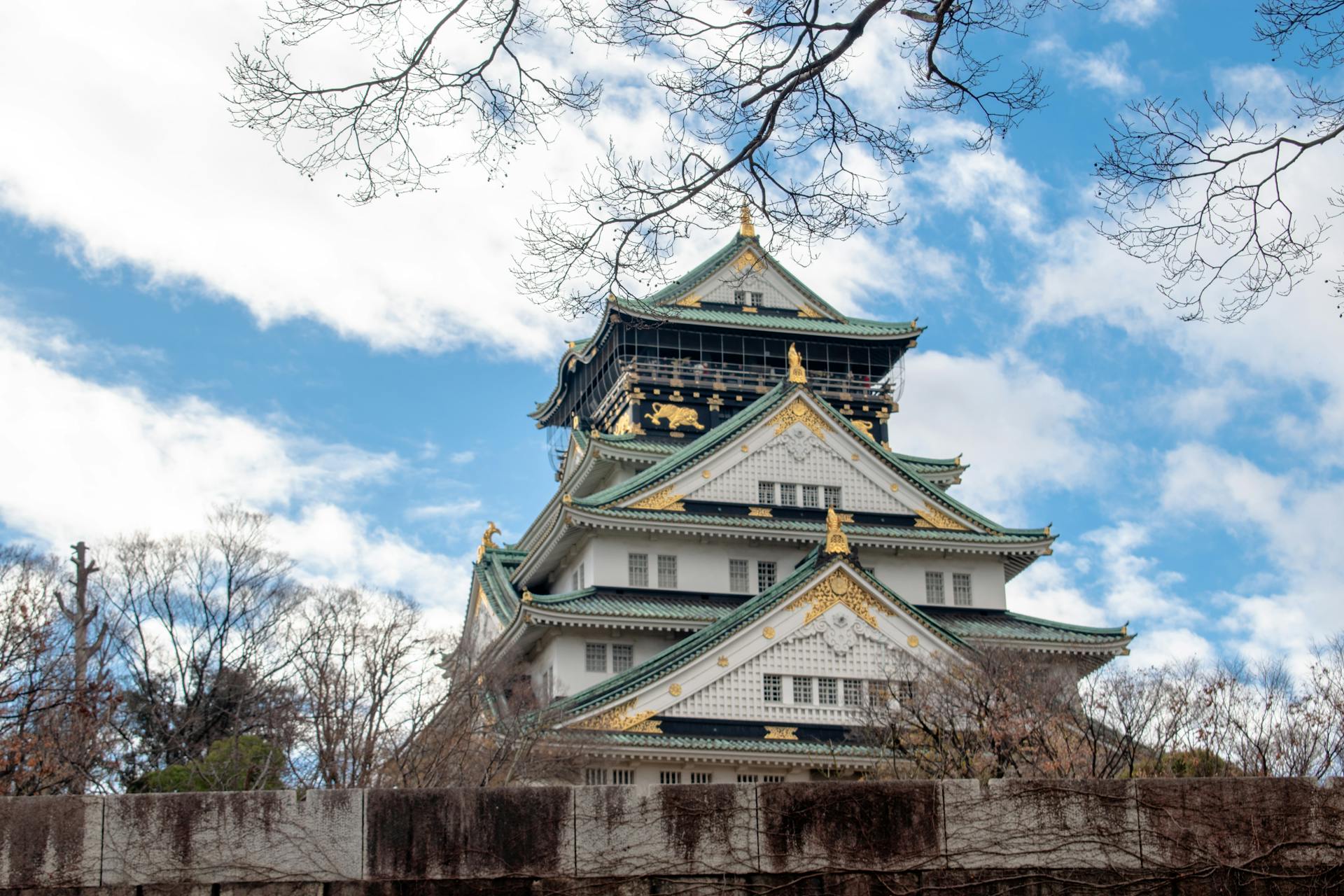 Osaka Castle with its ornate architecture stands proudly against a backdrop of clear blue skies and bare trees.