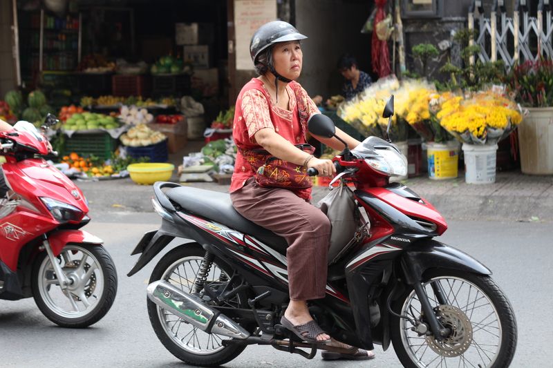 A woman riding a motorcycle past a market in Saigon
