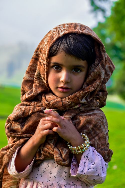Free A young girl in traditional attire stands gracefully against a lush green forest landscape. Stock Photo