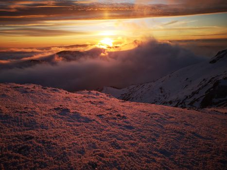 Breathtaking view of a sunset over snow-covered mountains with vibrant orange sky.