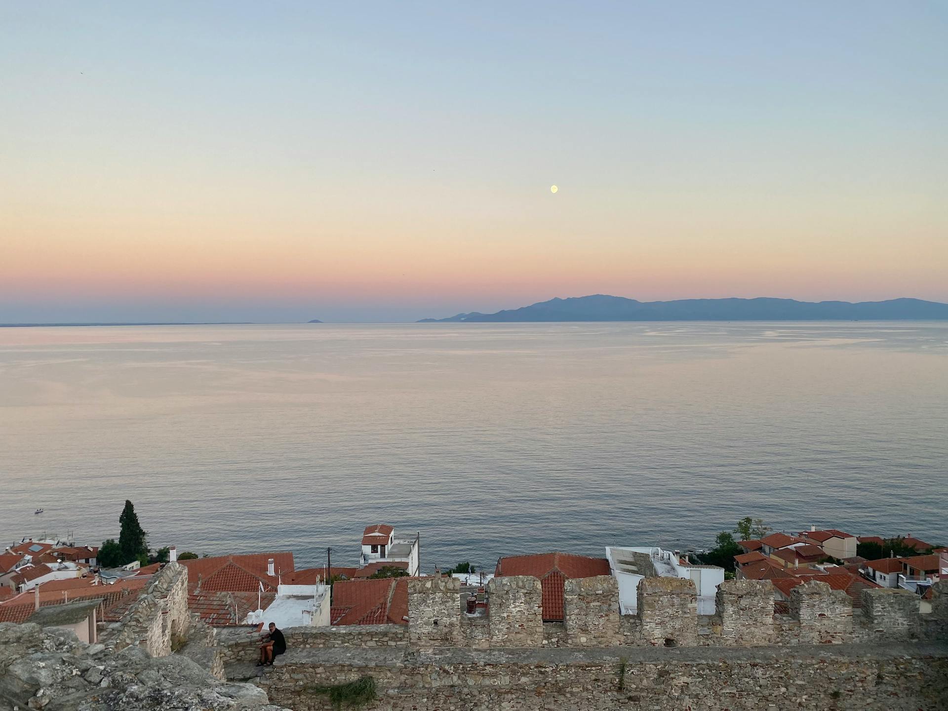 Beautiful sunset view over a Greek coastal village with sea and mountain backdrop.