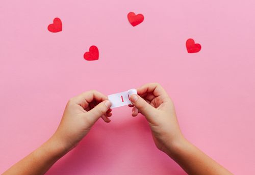 Free Hands holding a message with red hearts on a pink background, symbolizing love. Stock Photo
