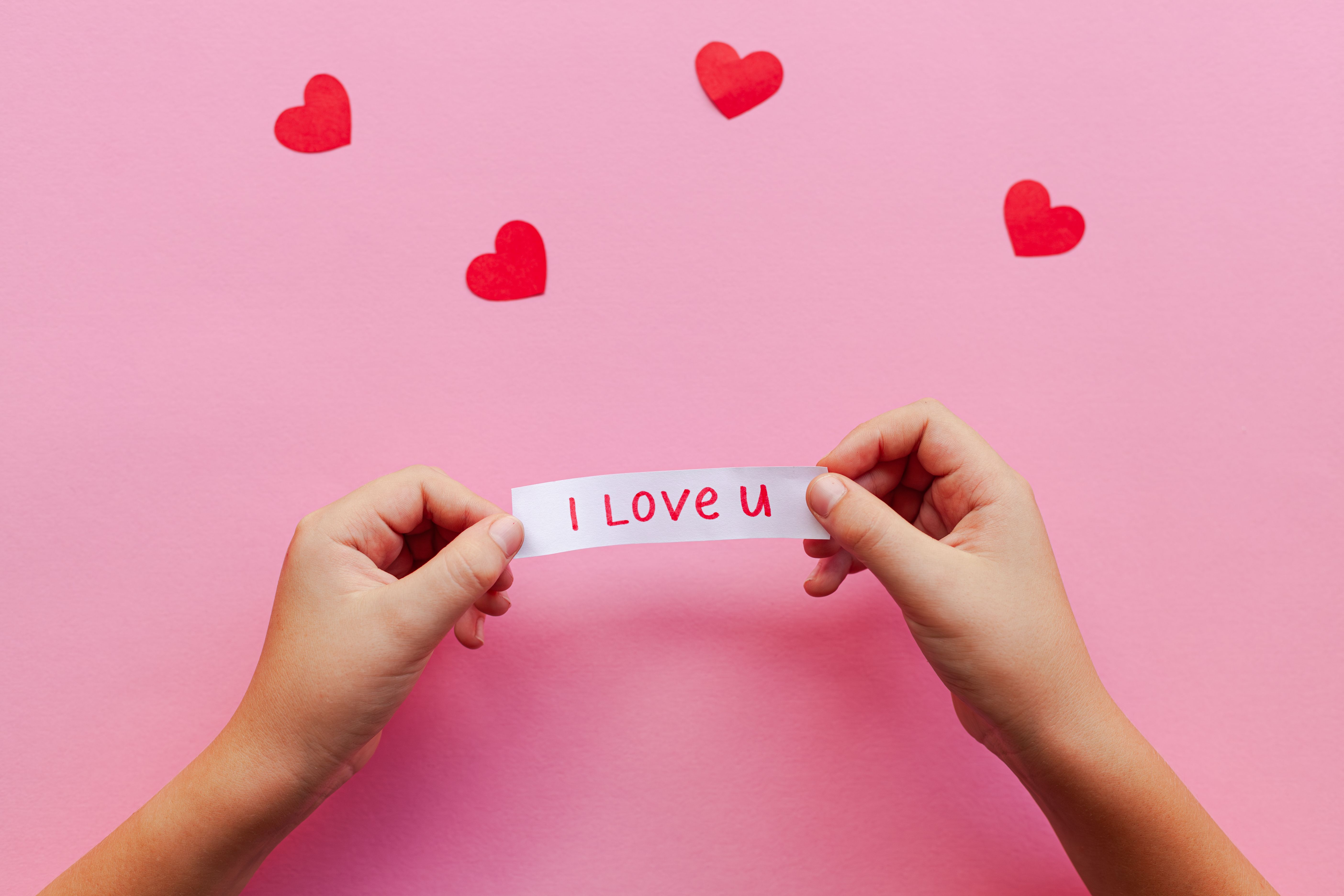 Gratuit Mâinile ținând un bilet „I Love U” pe un fundal roz cu inimioare roșii. Perfect pentru temele de Valentine's. Fotografie de stoc