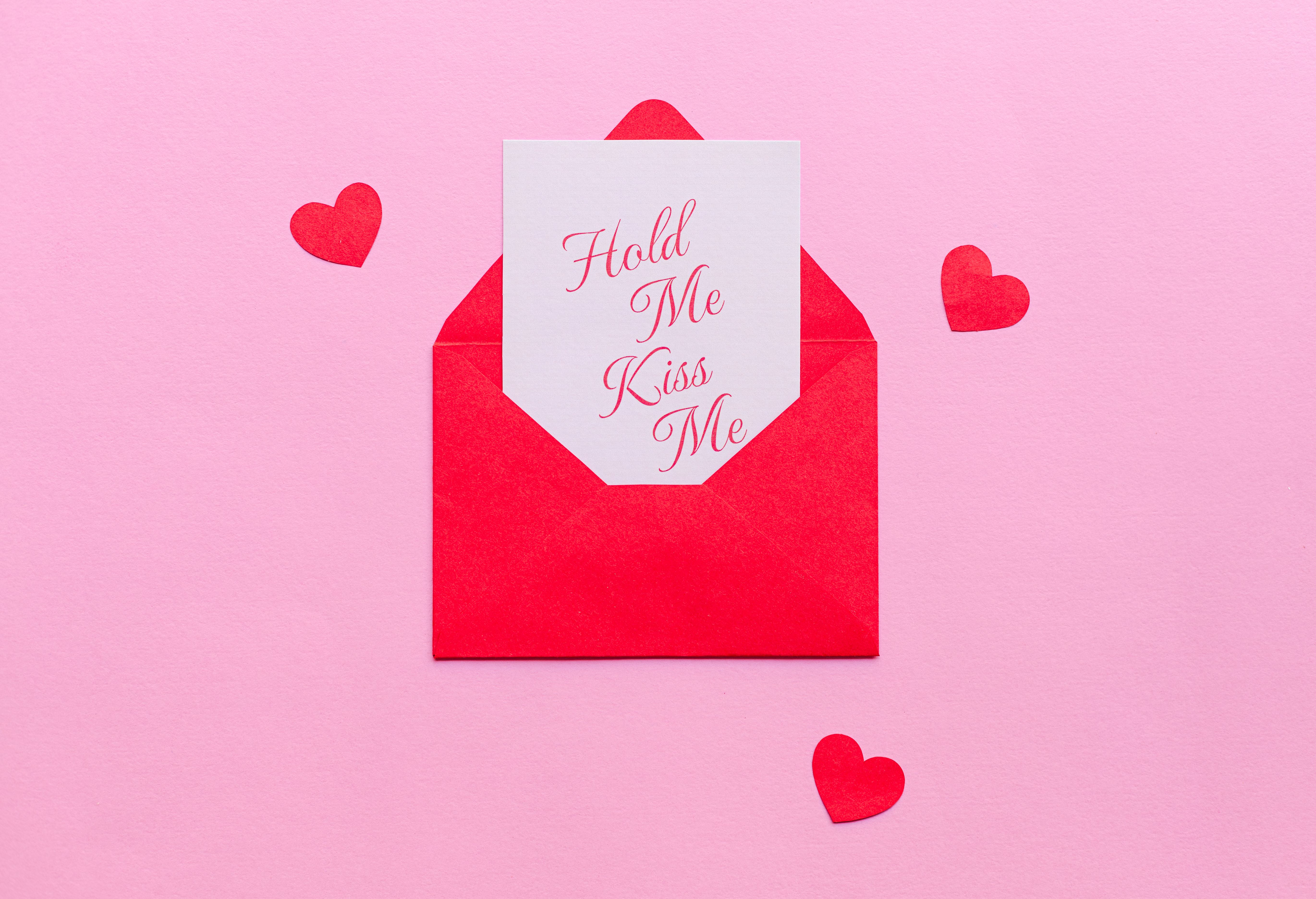 Red envelope with romantic card on a pink background, perfect for Valentine's Day.