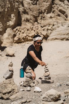 Woman stacking stones in a sunlit desert environment, enjoying an outdoor activity. by Ricky Esquivel