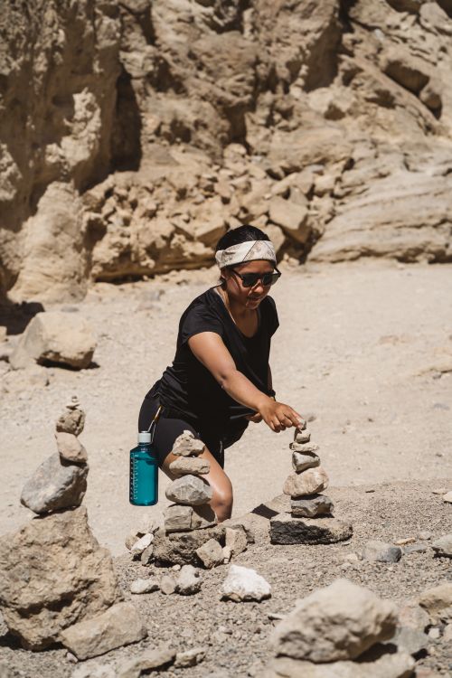 Free Woman stacking stones in a sunlit desert environment, enjoying an outdoor activity. Stock Photo