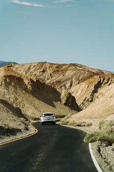 一辆汽车行驶在蜿蜒的沙漠道路上，头顶是晴朗的蓝天