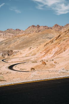 在蔚蓝的天空下，一条道路蜿蜒穿过干旱的沙漠山脉，非常适合旅行和冒险爱好者