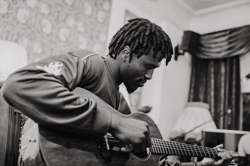 Free Moody black and white photo of a musician playing acoustic guitar in a classic room setting. Stock Photo