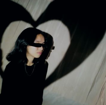 Stylish portrait of a person with heart-shaped shadow, wearing sunglasses indoors.