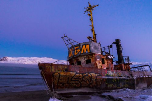 Free A dramatic shot of a rusted ship wrecked on the beach with snowy mountains in the background. Stock Photo