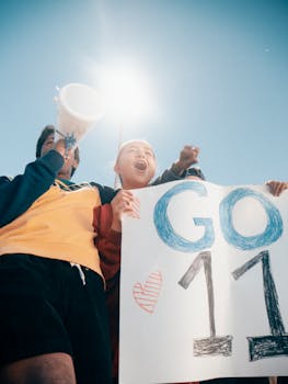 Group of enthusiastic people cheering outdoors, holding a sign with 'GO 11' under bright daylight.