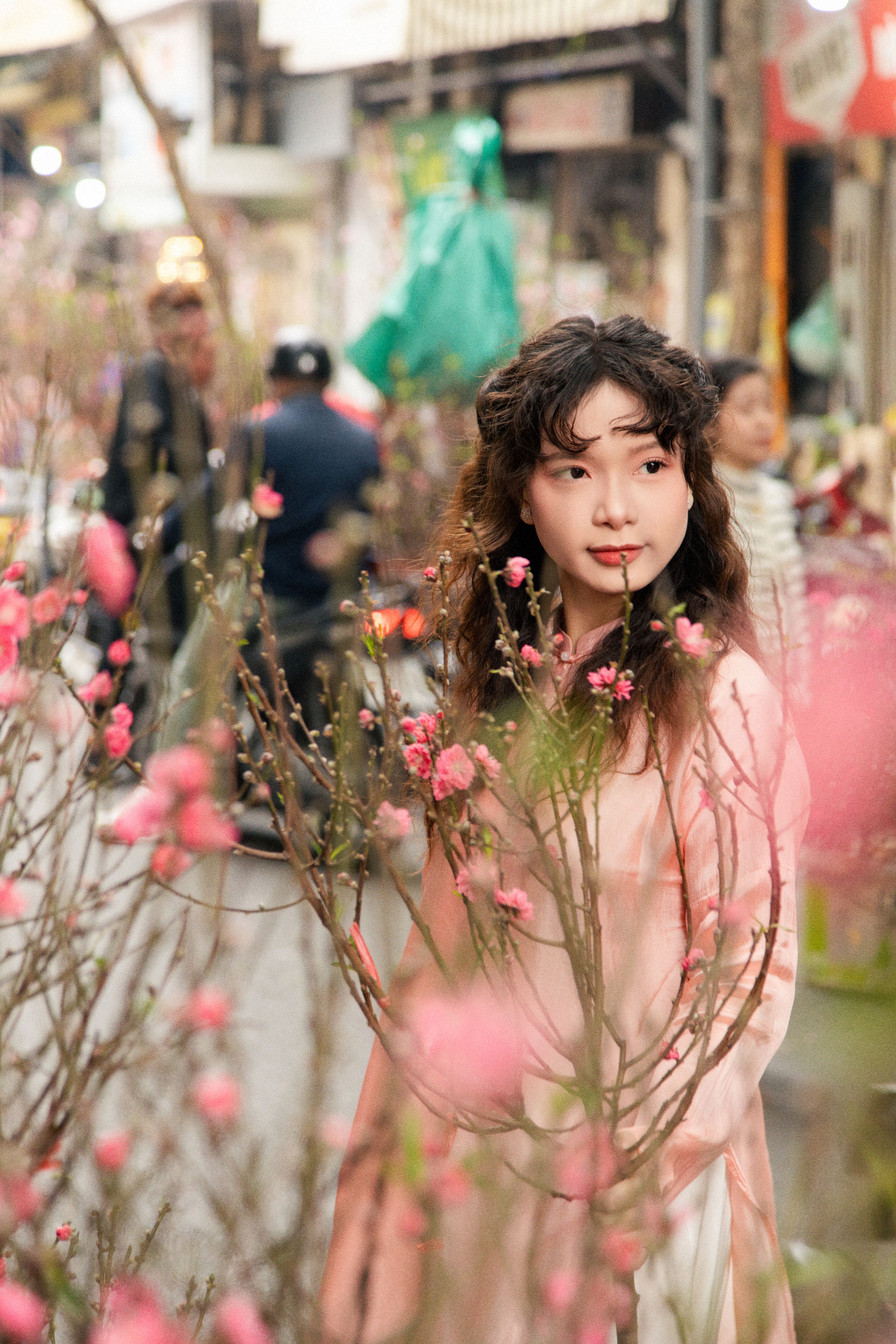 Portrait of a woman in Vietnamese market with peach blossoms during spring festival in Hanoi.