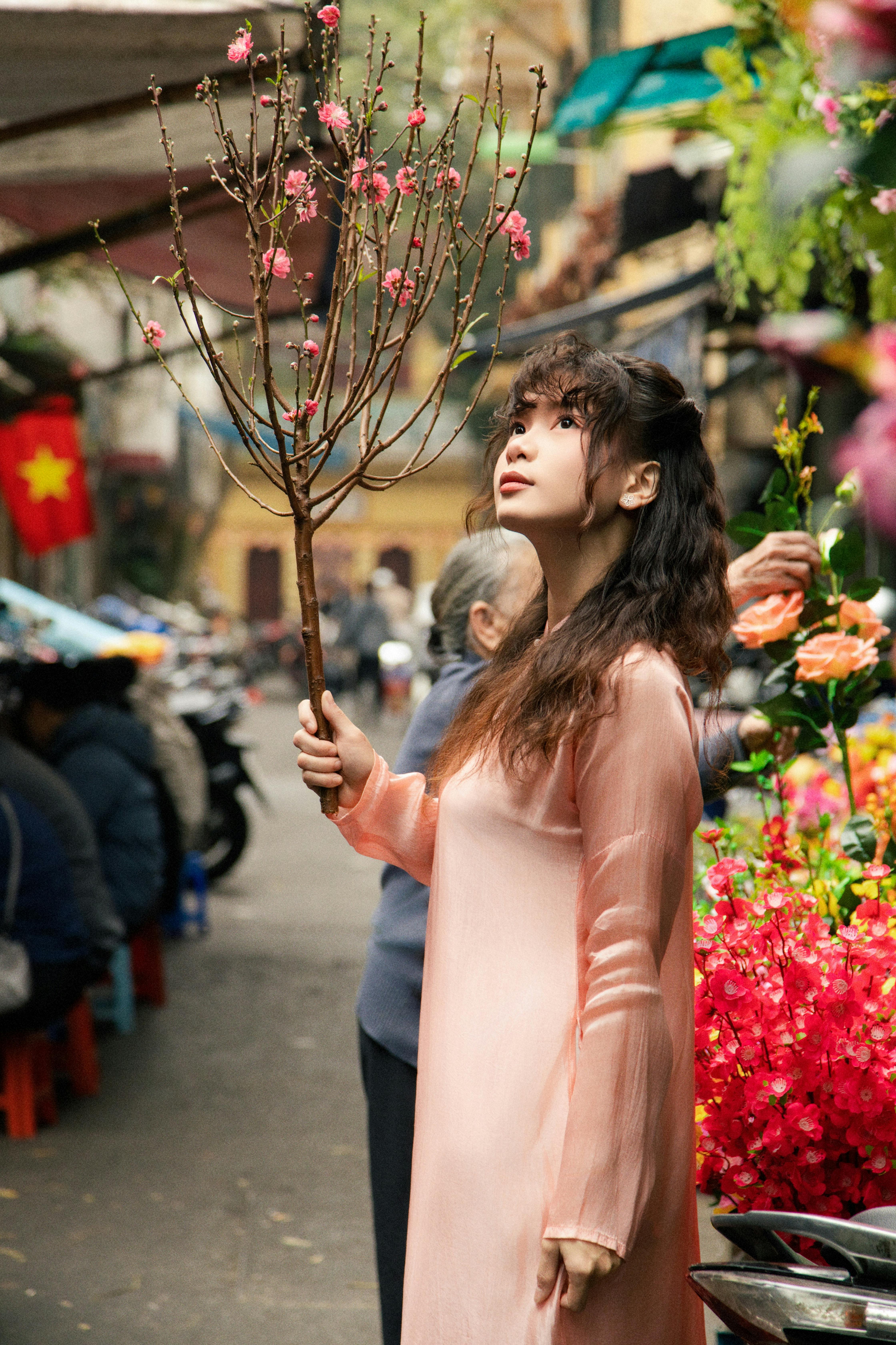 A young woman in Vietnam holding peach blossoms at a vibrant Hanoi flower market.