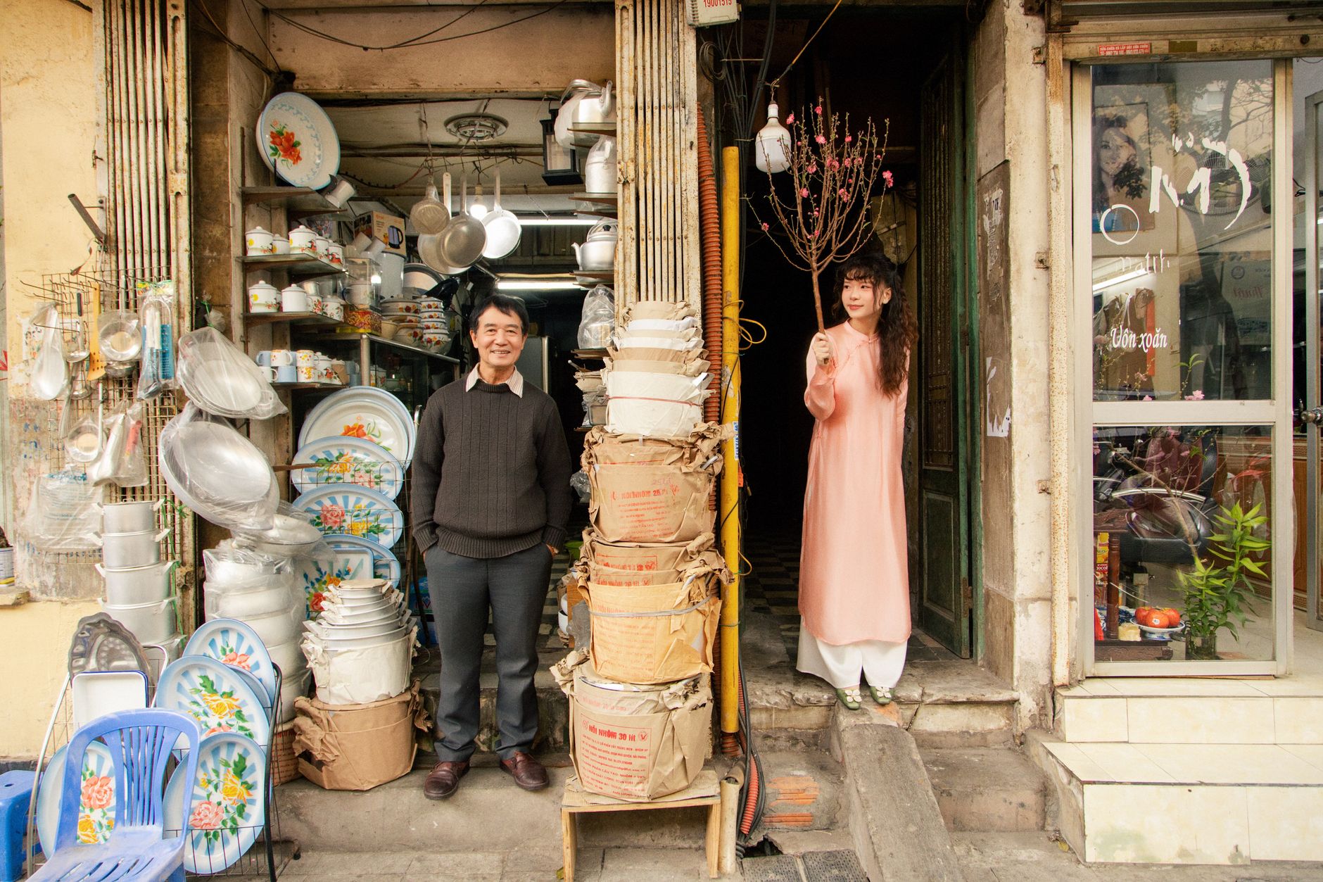 A Vietnamese man and woman in traditional attire at a shopfront in Hanoi, celebrating Tet.