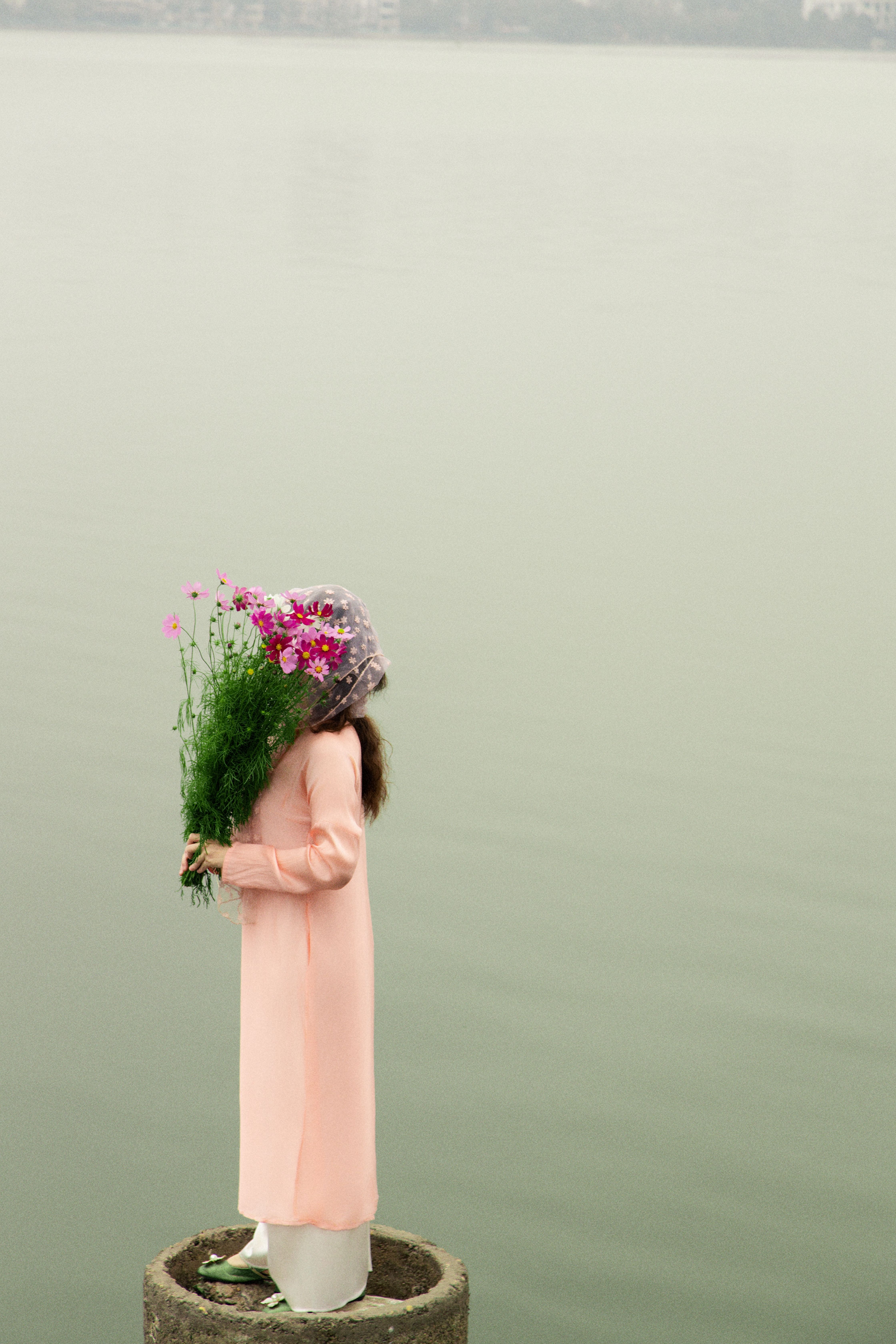 A serene image of a woman in traditional attire holding flowers, standing by a lake in Hanoi, Vietnam.