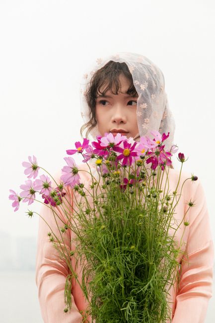 Young woman in Hanoi holding cosmos flowers, evoking a spring theme with soft tones and traditional attire.