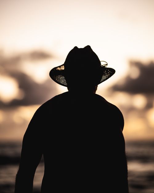 Free A captivating silhouette of a person in a hat against a stunning ocean sunset. Stock Photo