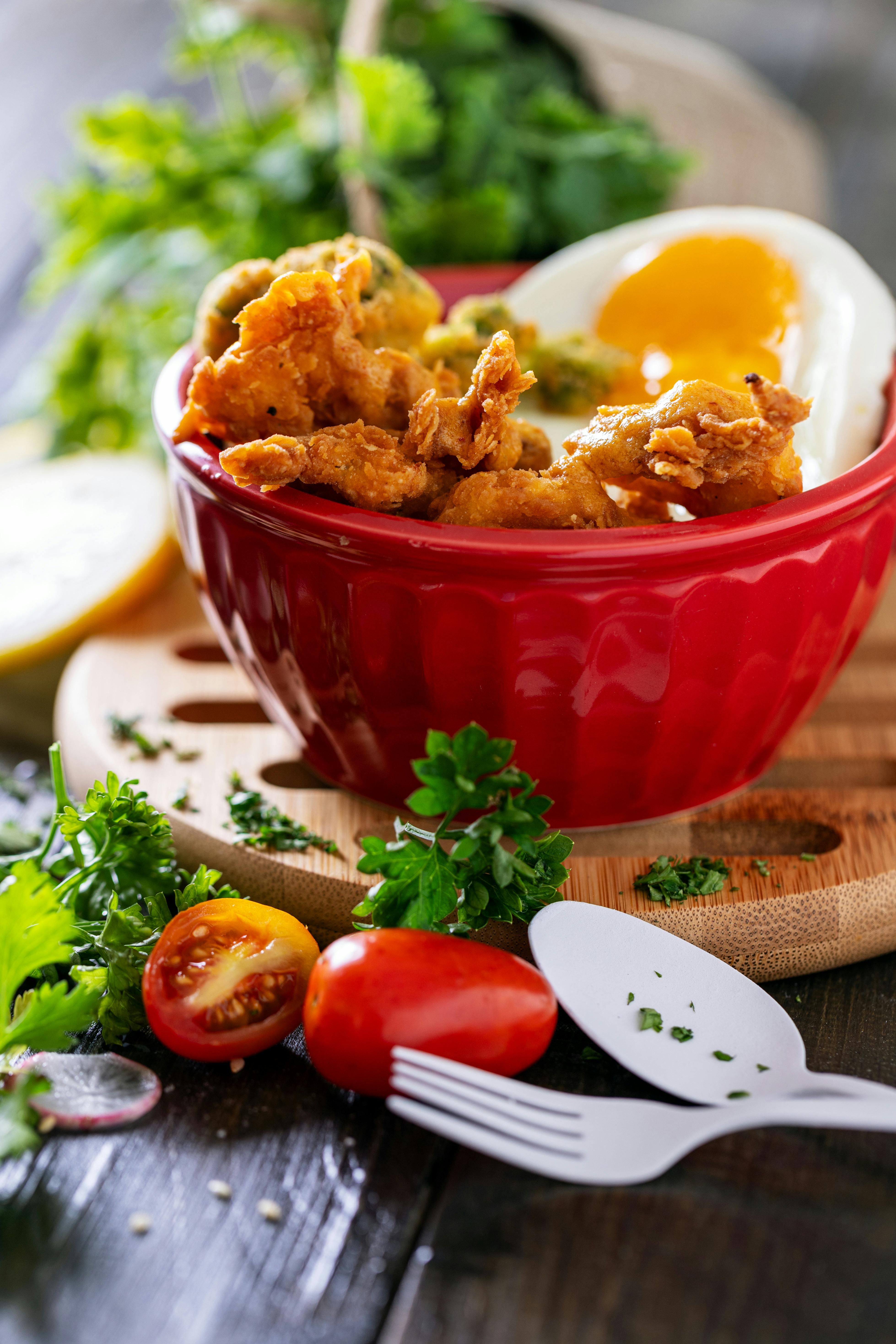 Tasty fried chicken and fresh vegetables served in a vibrant red bowl.