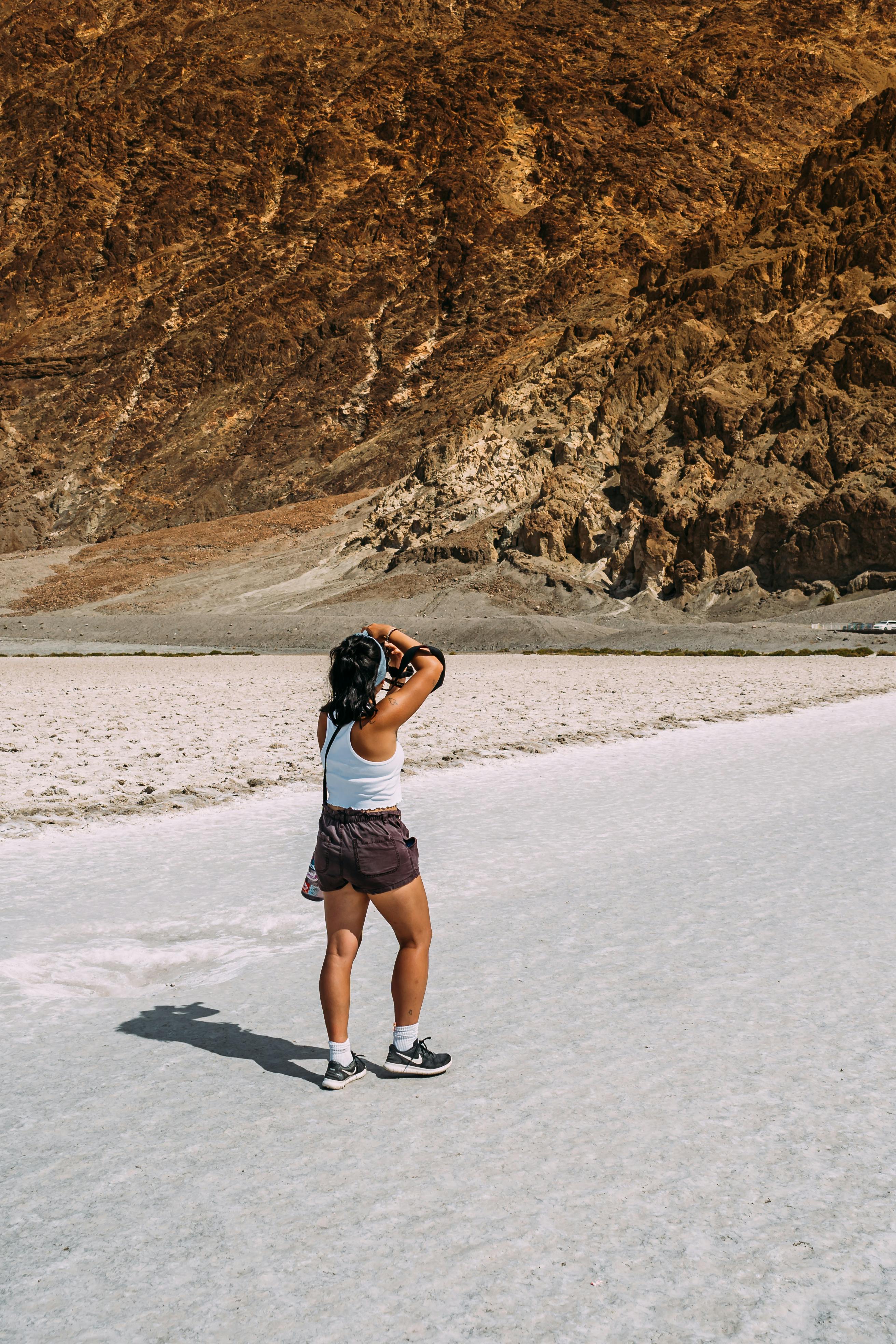 woman wearing white tank top and brown short shorts taking photo of brown cliff