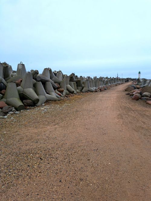 Free A serene path by the coast lined with tetrapods and rocks under a cloudy sky. Stock Photo