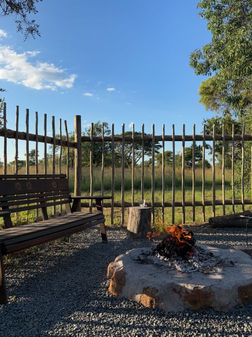Free A tranquil outdoor firepit scene with wooden benches and a fence under clear skies. Stock Photo