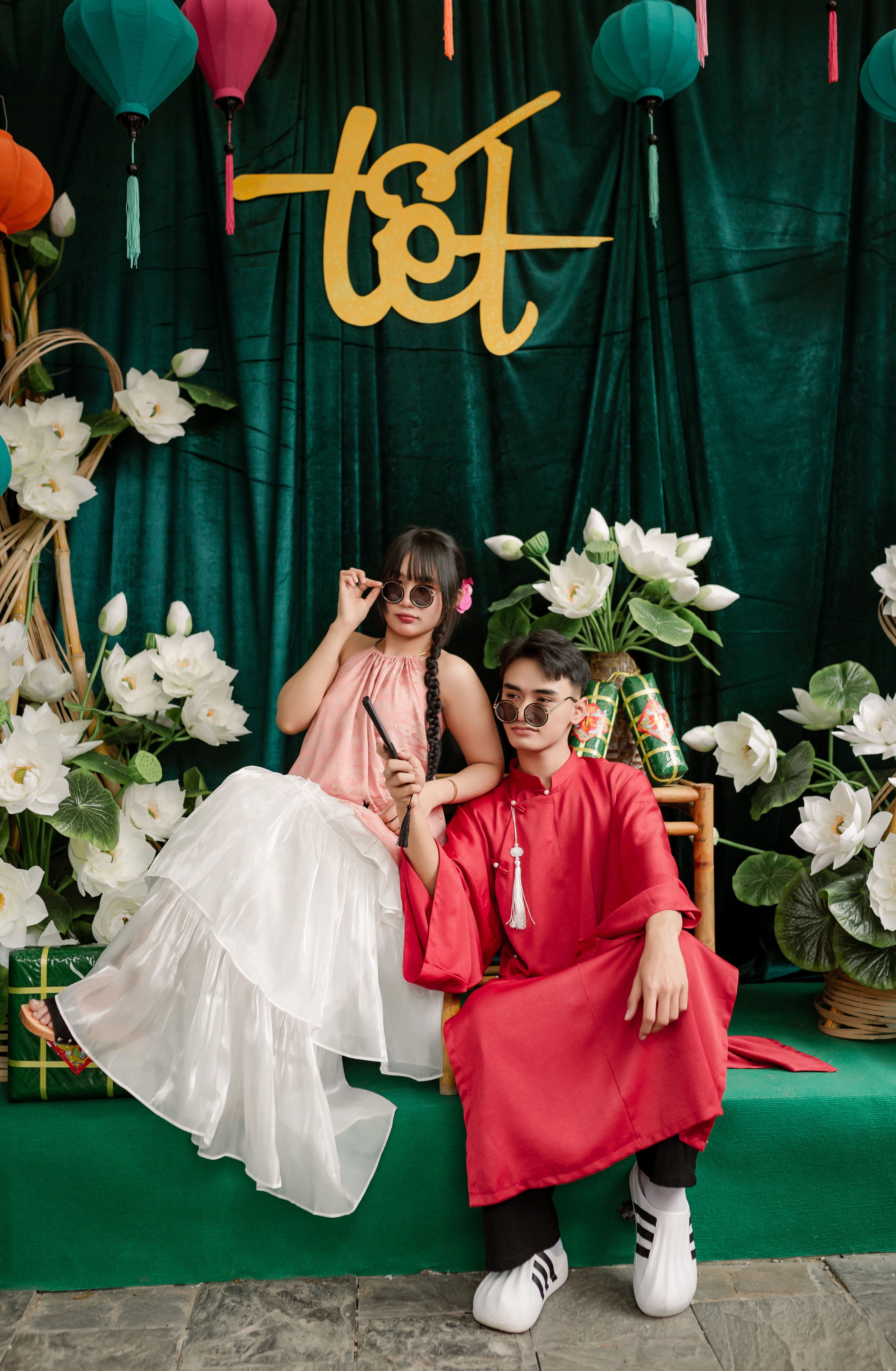 Two young adults in traditional Vietnamese attire enjoying Tết festival decorations with lotus flowers.