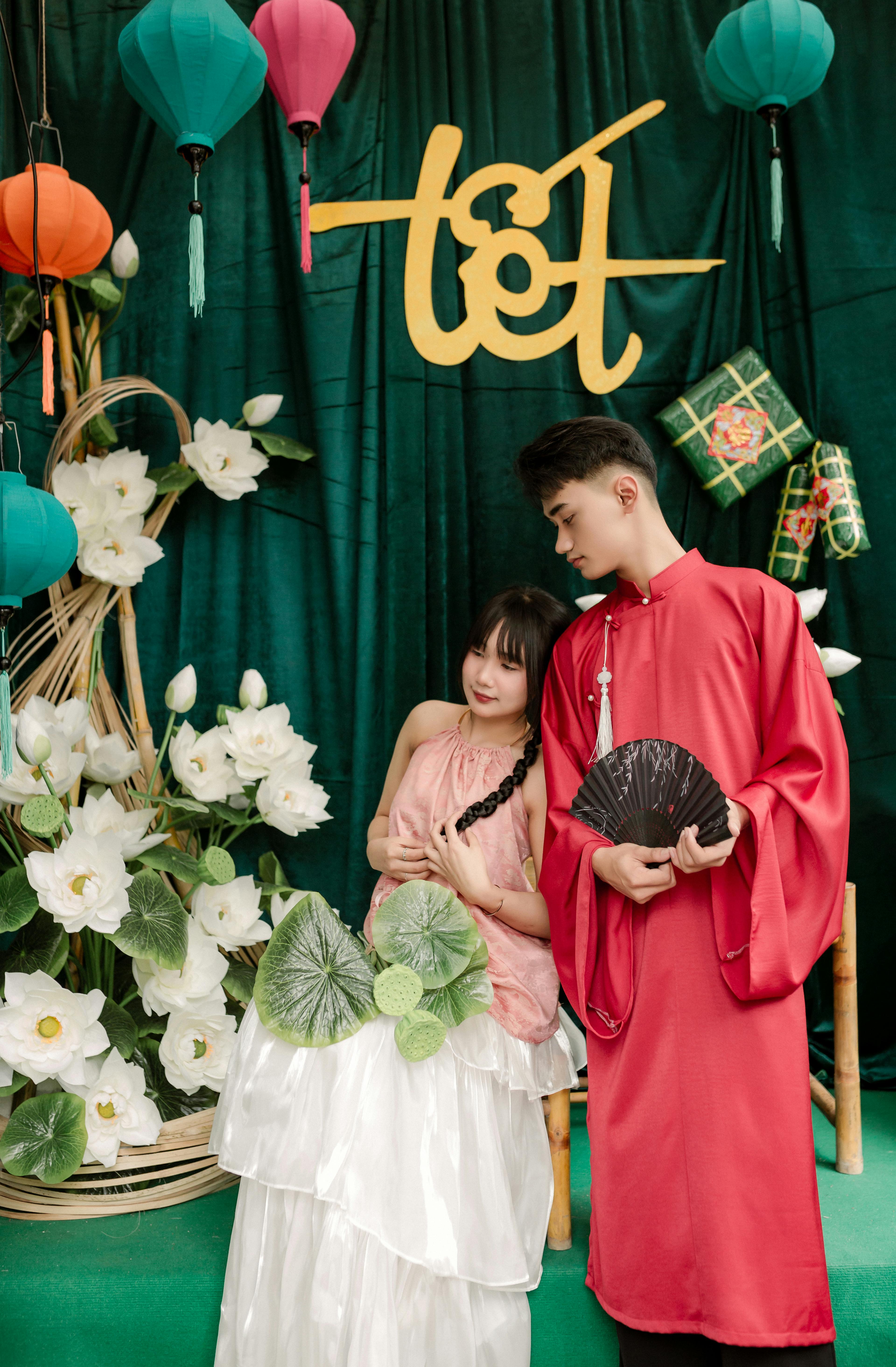 A couple celebrates Tet in Vietnam wearing traditional ao dai amidst lanterns and flowers.