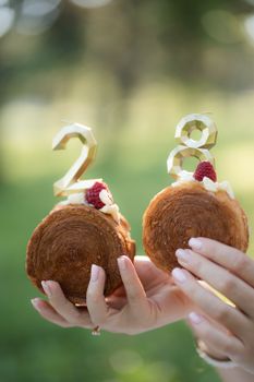 Two pastries with number toppers held outdoors, signifying a special occasion.