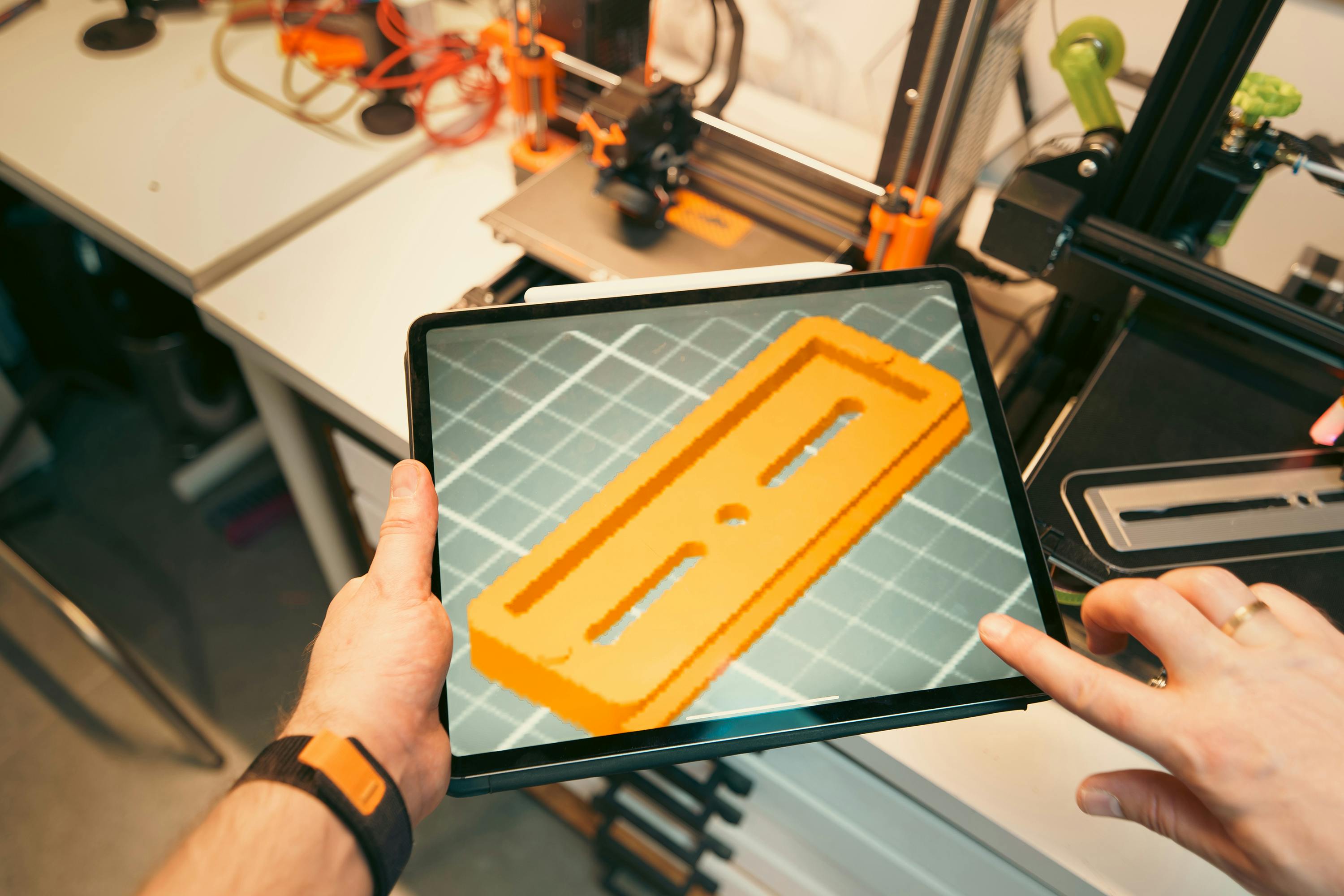bezplatná Osoba používá tablet k prohlížení prototypu 3D modelu v dílně vybavené 3D tiskárnami. Základová fotografie