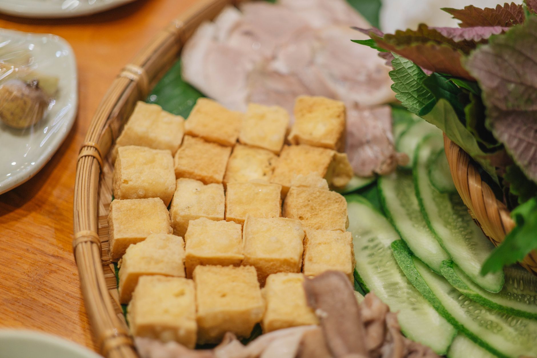 Delicious Vietnamese platter with tofu, cucumber, and herbs on a wooden table.