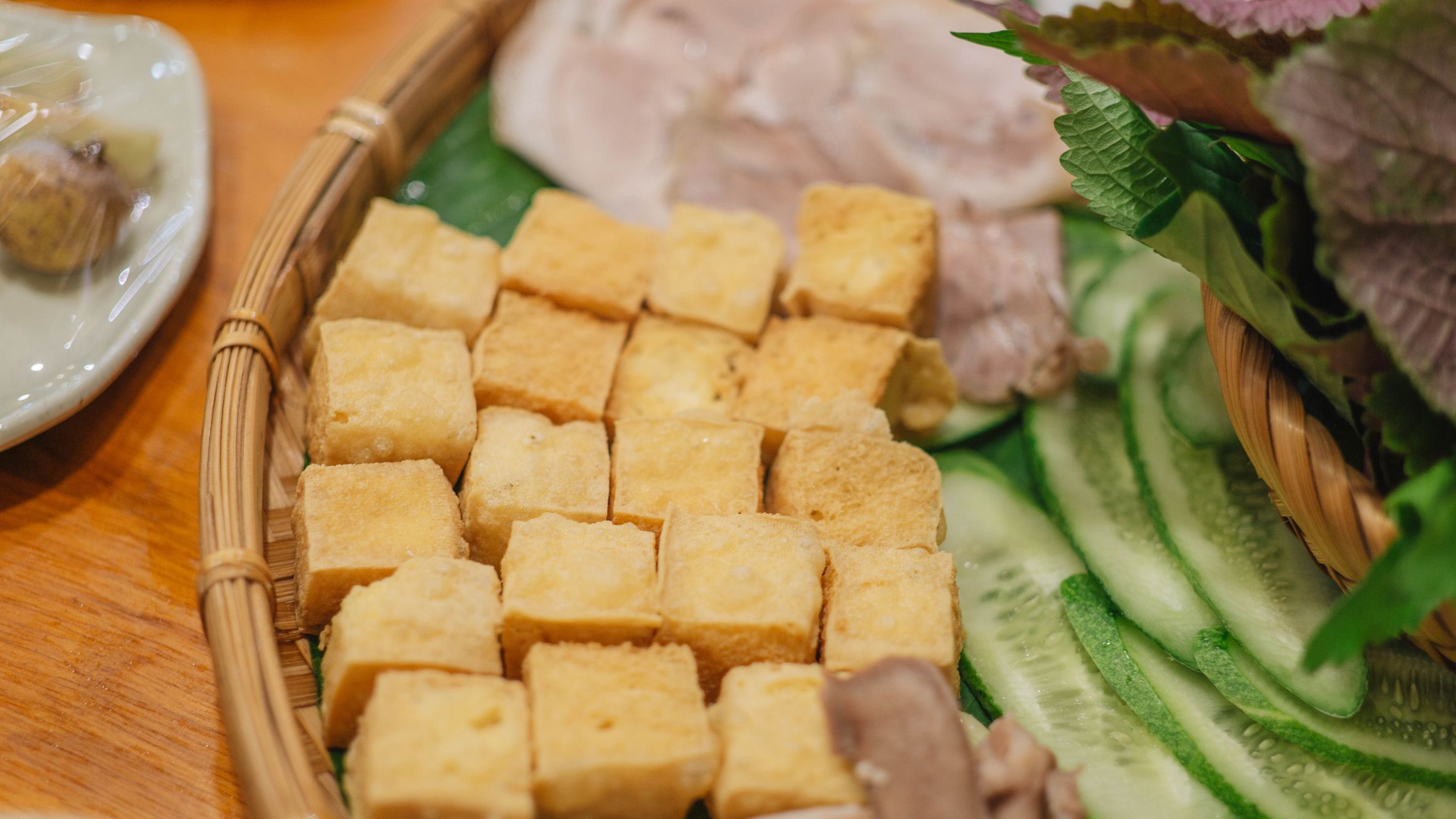 Delicious Vietnamese platter with tofu, cucumber, and herbs on a wooden table.