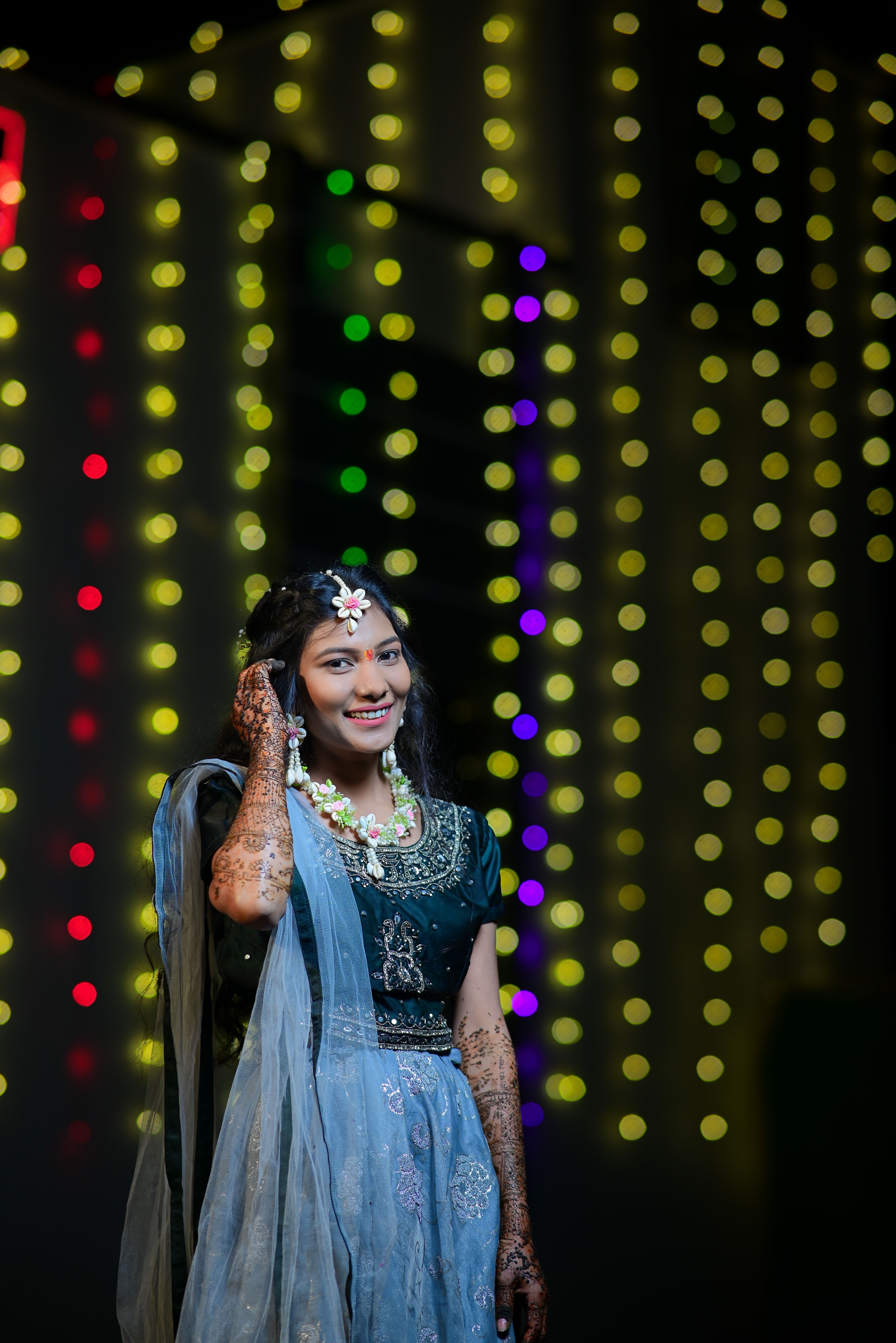 Beautiful Indian bride in traditional attire with henna, against a backdrop of colorful lights.