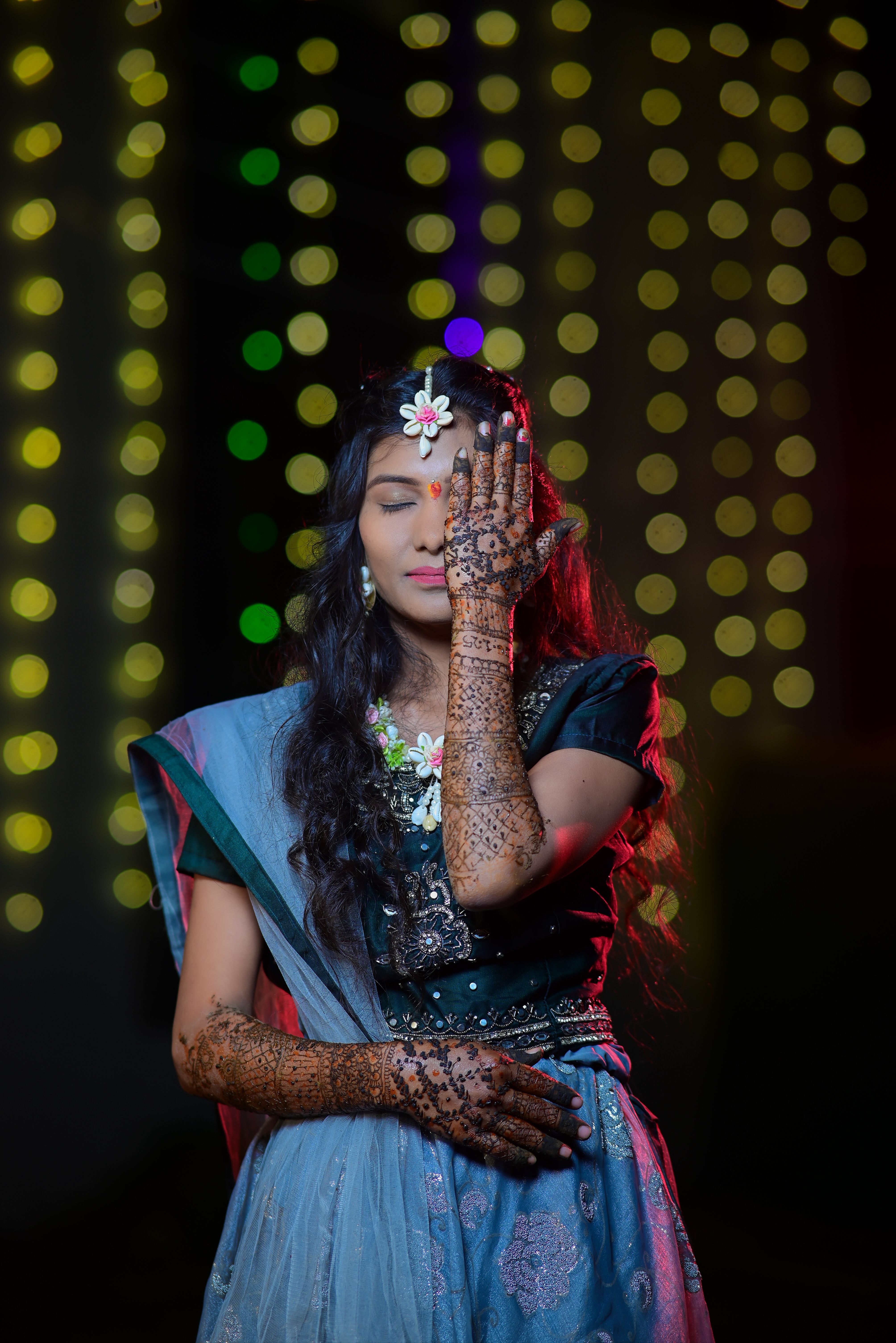 Indian woman with henna in traditional attire against colorful lights background.