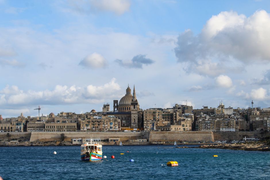 Panoramic view of Valletta's historic skyline with boats at sea under a vibrant blue sky.