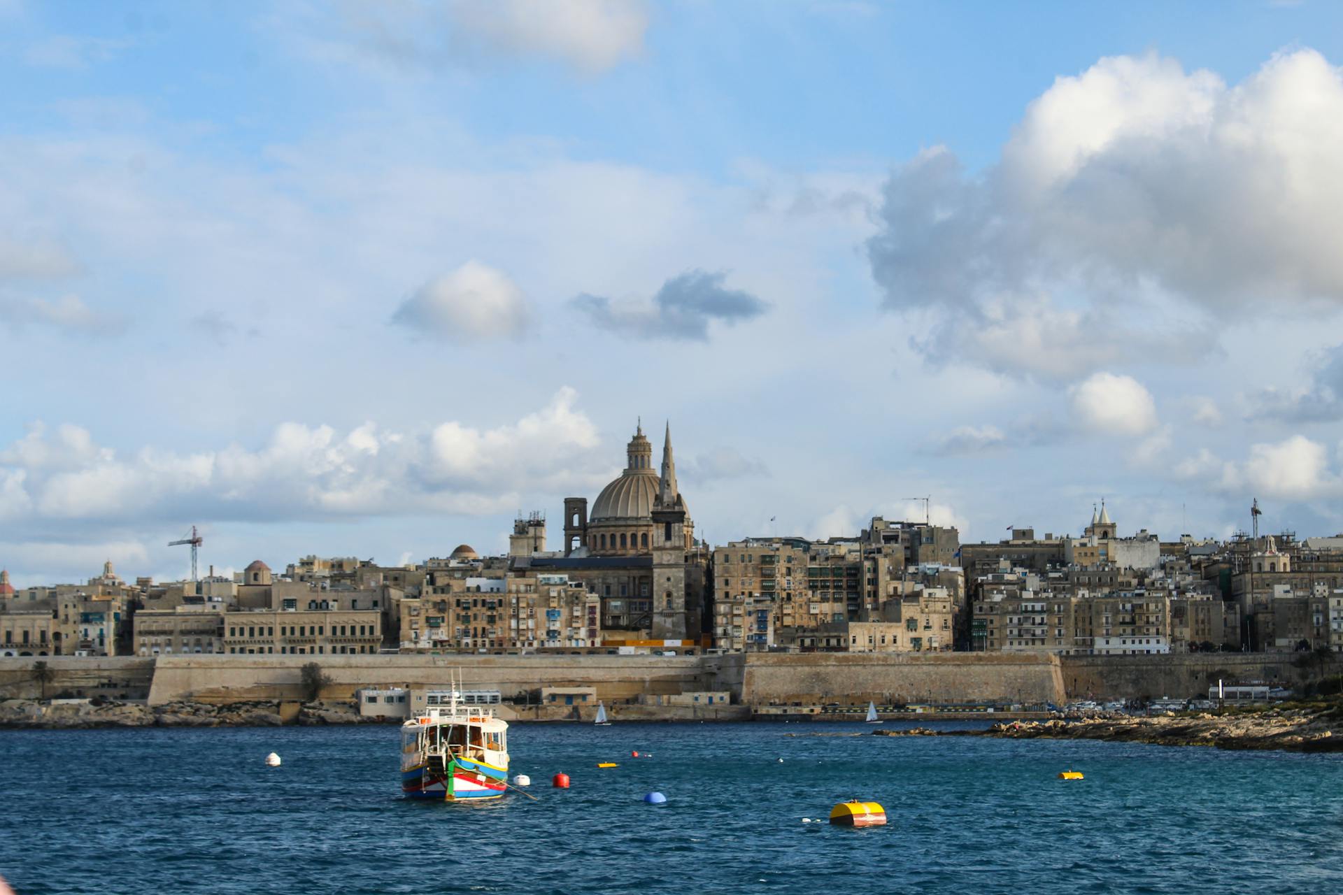 Panoramic view of Valletta's historic skyline with boats at sea under a vibrant blue sky.