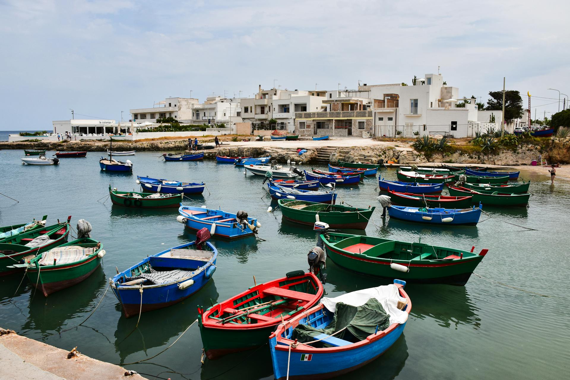 Vibrant fishing boats in a serene harbor of Apulia, Italy against a backdrop of white coastal buildings.