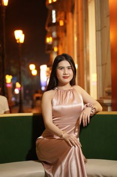 Stylish woman in a satin dress posing on a city street at night.