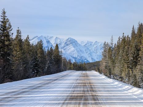 Serene winter view of a snow-covered road with majestic mountains in Jasper, AB.