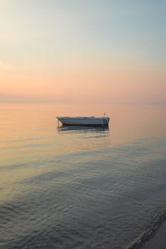 A solitary boat floating on calm waters during a serene sunset, creating a peaceful and tranquil seascape.