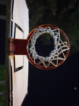 Close-up of a basketball hoop with net at night on outdoor court.