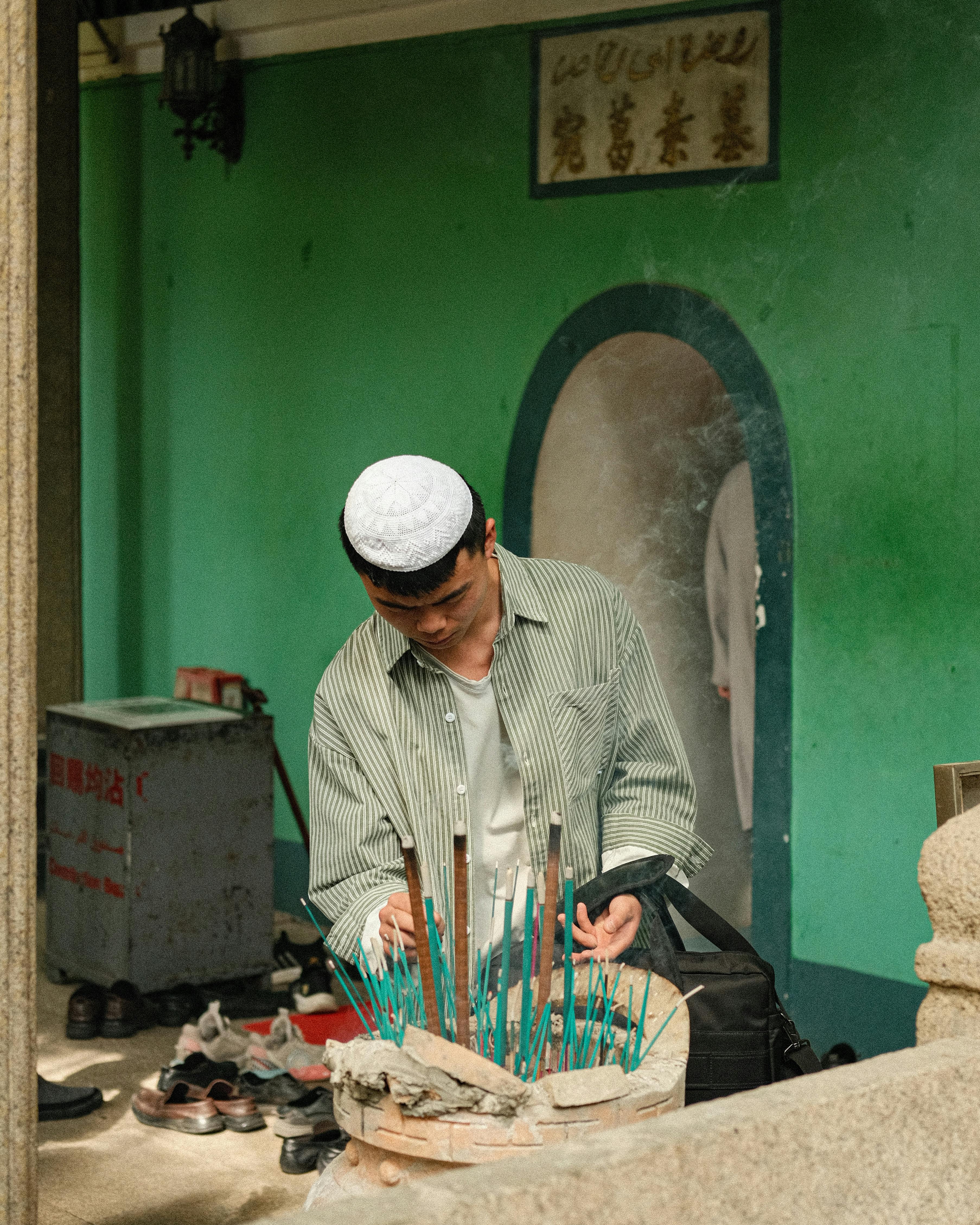 A man lighting incense sticks at a religious site with cultural attire.