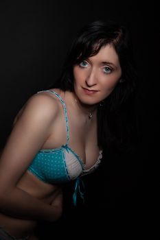 Intimate portrait of a woman posing in blue polka dot lingerie with dark background.
