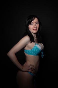 Elegant woman posing in blue polka dot lingerie against a dark background.
