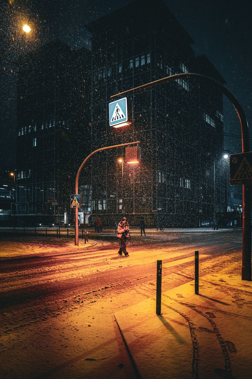 An atmospheric snowy street scene in Berlin captured at night with glowing streetlights.